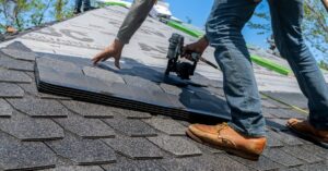 Roofer using nail gun for shingle installation on residential roof.